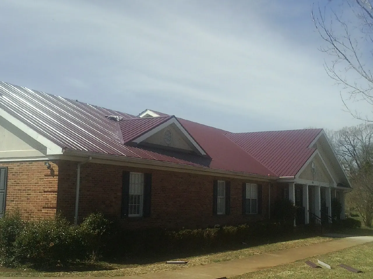 Red metal roof with gabled entries on a long brick building, from a Hail Damage Roof Repair job in Bellevue