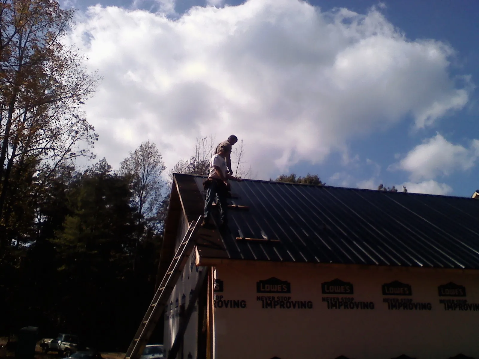 Roofer fastening dark metal panels high against a cloudy sky in Bellevue